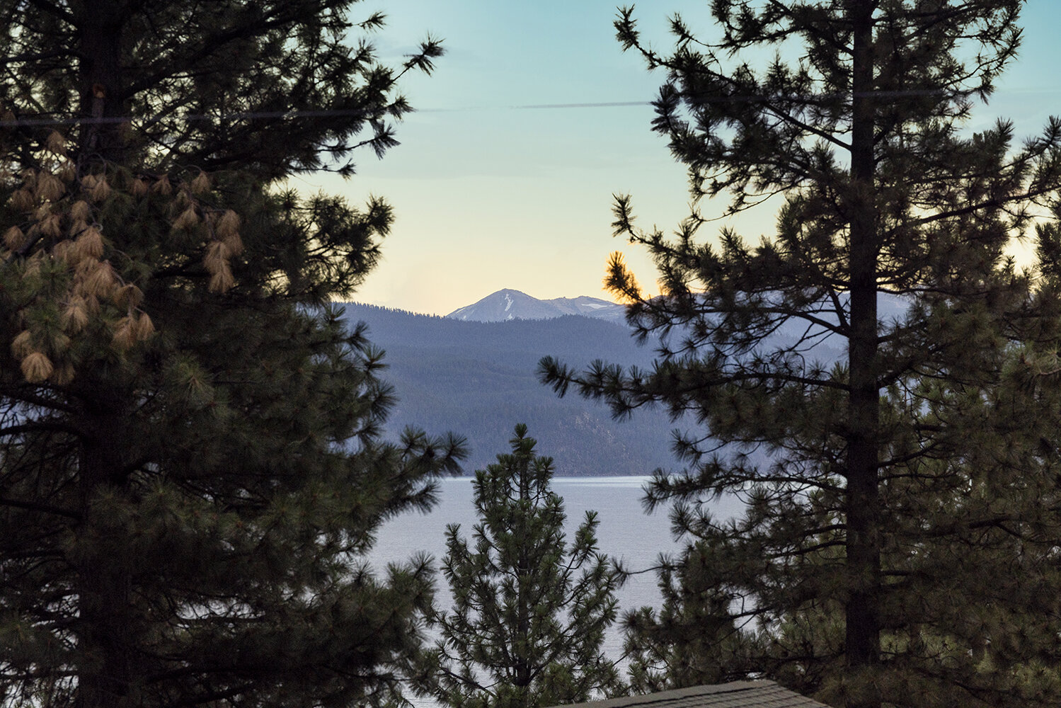 Lake Tahoe and the Sierra peaks at dusk, seen through the pines from the Kinpine House deck