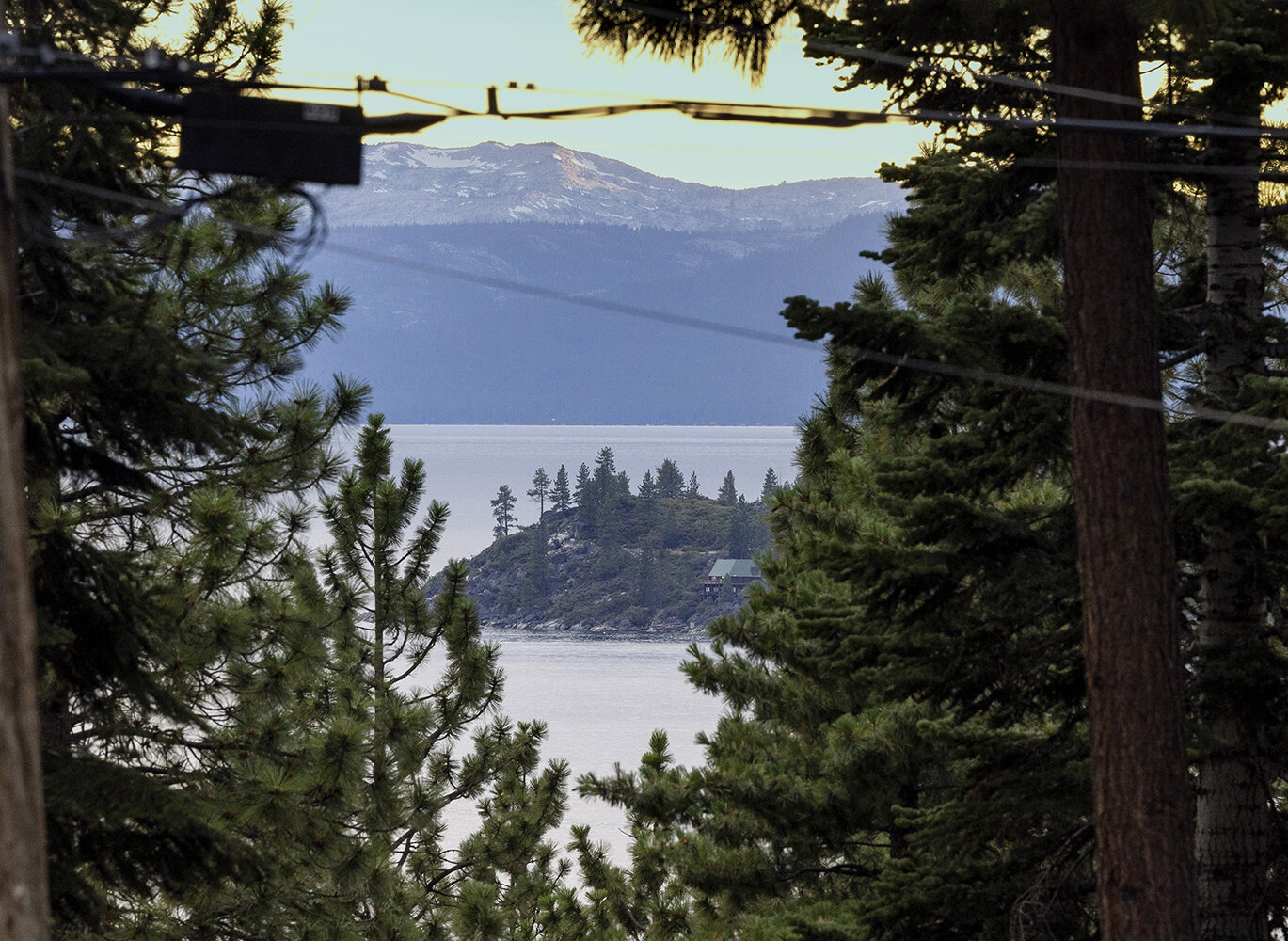 A wooded point on Lake Tahoe seen between pine trunks at dusk